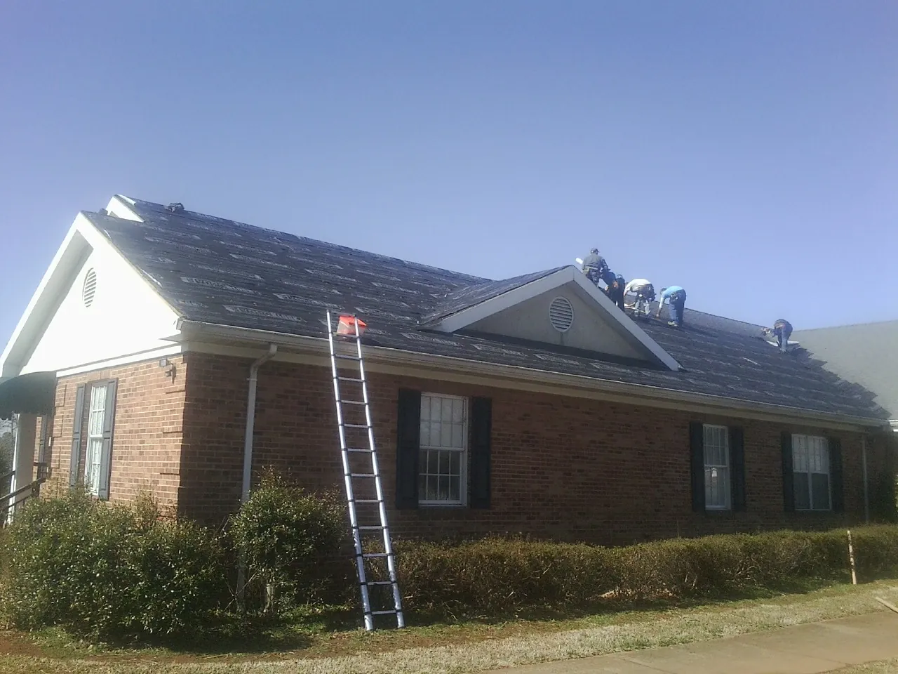 Crew tearing shingles off a brick ranch roof with a ladder set — Emergency Roof Repair work by our crew in Bowers