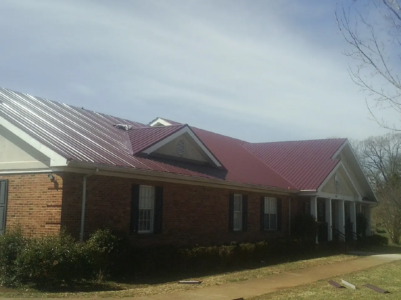 Red metal roof with gabled entries on a long brick building, from a Hail Damage Roof Repair job in Bowers
