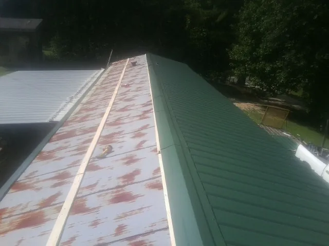 Old rusted panels beside newly installed green metal roofing — Wind Damage Roof Repair by Roofing Brothers in Bowers