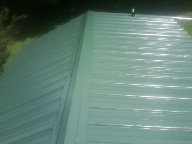 New green metal panels meeting at the ridge of a roof — Flat Roof Repair work by our crew in Bowers