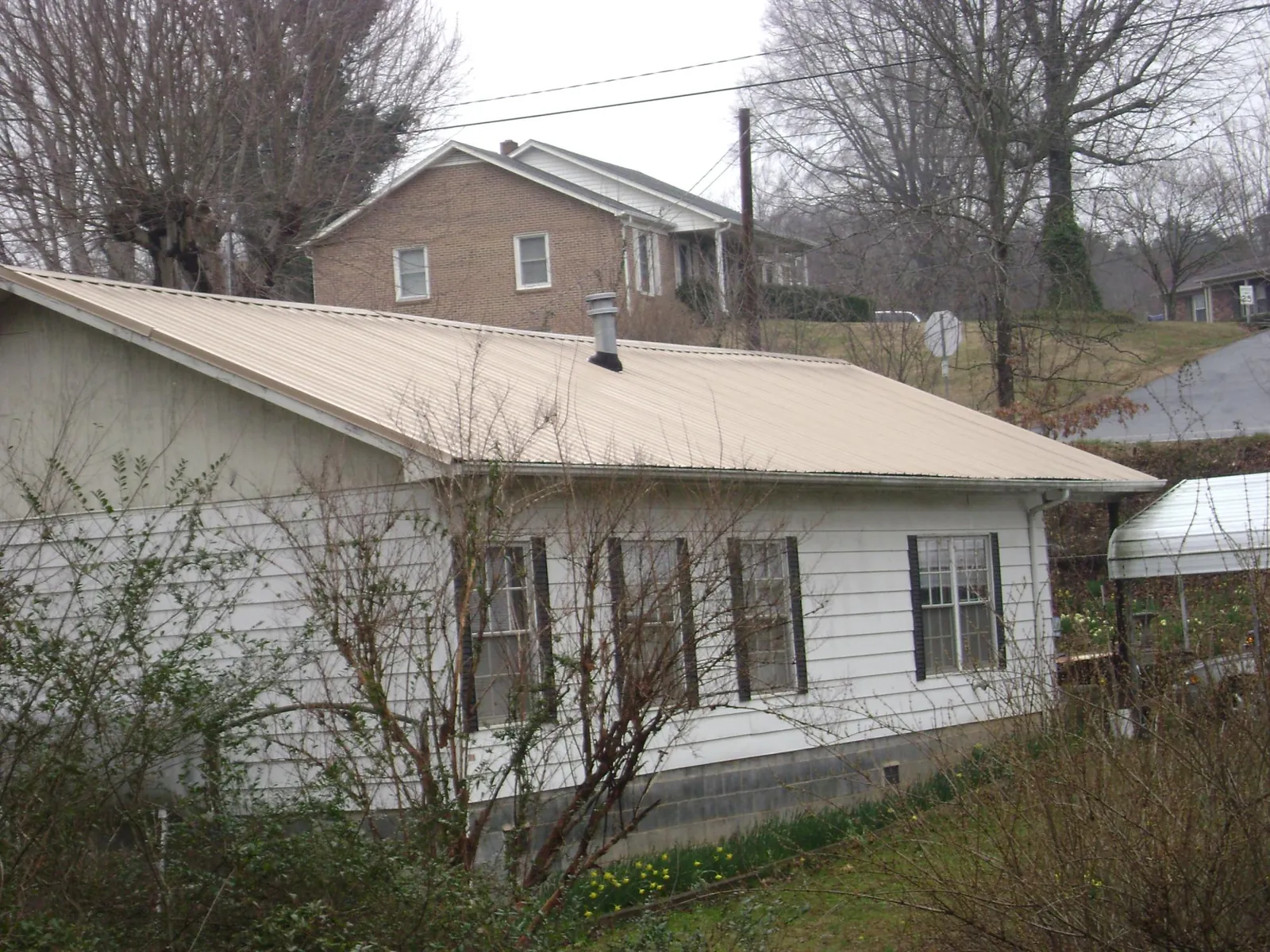 Tan metal roof on a white sided house set into a hillside — Commercial Roofing by Roofing Brothers in Bowers