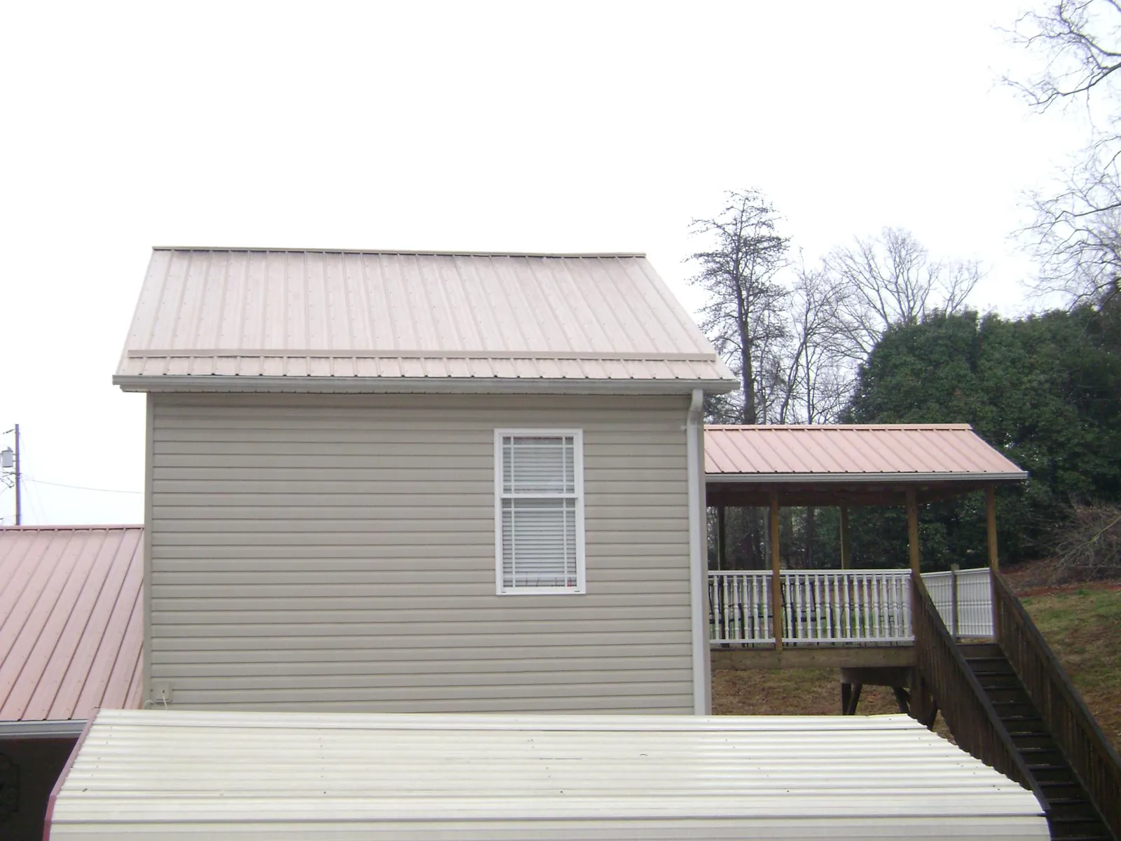 Tan metal roofs on a two story addition and attached porch, from a Roof Replacement job in Bowers
